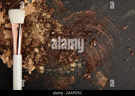 Pinceau maquillage blanc et brun et or fards à paupières organisé sur une pierre. Banque D'Images