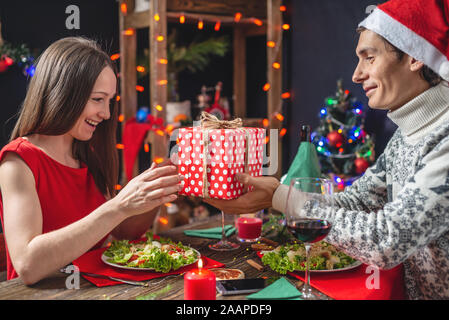 Un homme tient une boîte-cadeau pour sa bien-aimée. Un jeune beau couple amoureux de passer un dîner de fête dans les décorations de Noël Banque D'Images