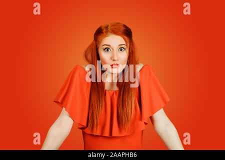 À la femme coupable confus en haussant les épaules dans la confusion. Jeune rousse dame portant robe rouge et jaune isolé sur fond rouge maquillage Banque D'Images