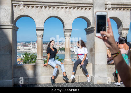 Une paire de femmes s'asseoir sur un balcon à l'Halaszbastya et poser pour une photo avec les toits de Budapest dans l'arrière-plan, Budapest, Hongrie Banque D'Images