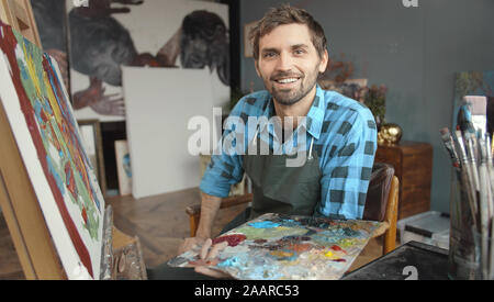 Portrait de jeune beau mâle artiste au travail assis au chevalet avec une palette Banque D'Images