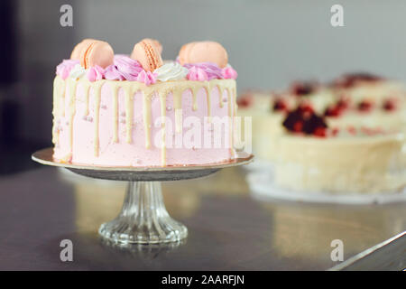 Gâteau rose décoré de macarons sur la table. Banque D'Images
