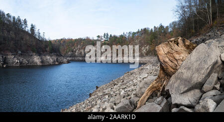 Rippled water surface bleue dans une rivière tour. La sécheresse en paysage d'automne. Vieille souche et des pierres sur une falaise rocheuse de la rive à découvert. Arbres en pente. Banque D'Images