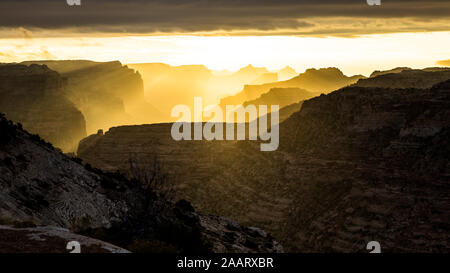 Lever du soleil dans le désert de l'Utah jusqu'éclairage des couches de falaise rocheuse de mesas, de buttes et de tours par rétro-éclairé à la lumière du matin. Banque D'Images