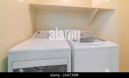 Cadre panoramique Lave-linge et sèche-linge dans une buanderie avec tablette et mur beige Banque D'Images