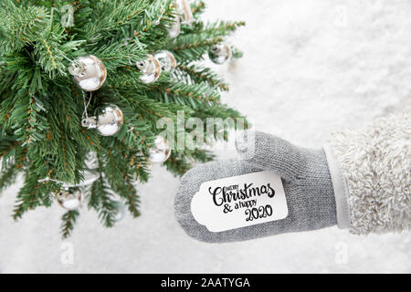 Gant avec étiquette avec calligraphie anglaise Joyeux Noël et une Bonne 2020. Arbre de Noël avec de la neige et de l'Ornement Silver Ball Banque D'Images
