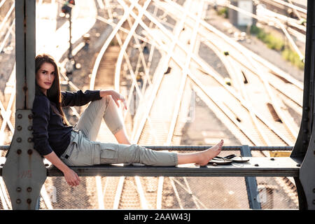 Jeune femme assise sur le pont de pirates au coucher du soleil, Munich, Allemagne Banque D'Images