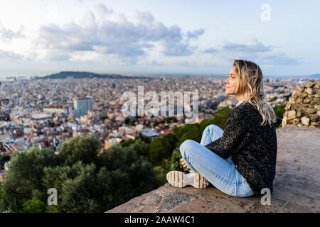 Jeune femme assise au-dessus de la ville au lever du soleil, Barcelone, Espagne Banque D'Images