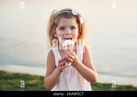 Une belle petite fille mange une glace près de l'eau Banque D'Images