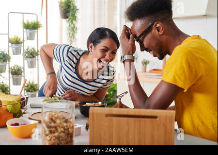 Couple laughing multiethnique, déjeunant ensemble dans la cuisine Banque D'Images