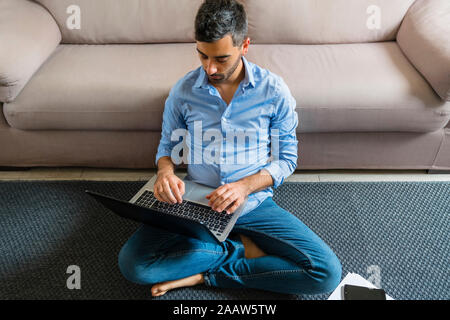 Jeune homme assis sur le plancher à l'aide d'ordinateur portable Banque D'Images