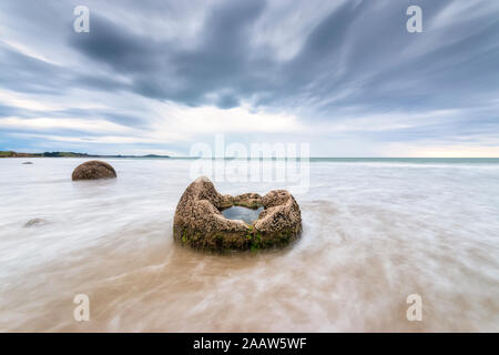 Moeraki Boulder en mer à Koekohe Plage contre ciel nuageux, Nouvelle-Zélande Banque D'Images