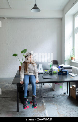 Fille avec patins à sitting on desk in office Banque D'Images