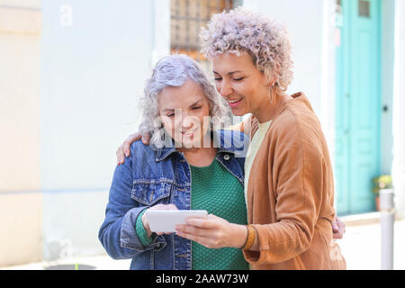 Maman avec ses supérieurs à l'aide de sa fille adulte smartphone outdoors Banque D'Images