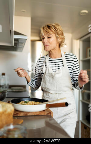 Femme mature plat de pâtes faites maison dégustation dans la cuisine à la maison Banque D'Images