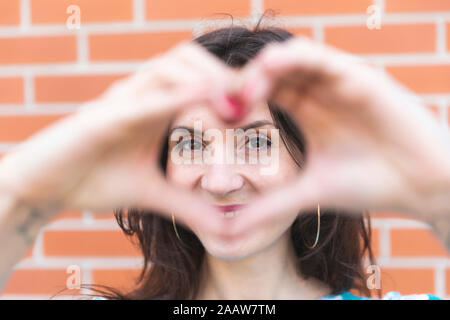 Portrait of smiling young woman looking at camera dans les mains en forme de cœur Banque D'Images