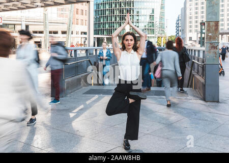 Young businesswoman pratiquant le yoga dans la ville à l'heure de pointe, Berlin, Allemagne Banque D'Images