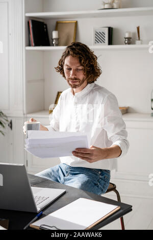 L'homme assis à table à la maison l'examen des documents de travail Banque D'Images