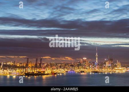 Les bâtiments modernes lumineux par mer contre ciel nuageux au crépuscule dans Auckland, Nouvelle-Zélande Banque D'Images