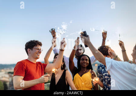 Groupe de professionnels multi-ethnic friends célébrer une fête dans la soirée, holding sparklers Banque D'Images