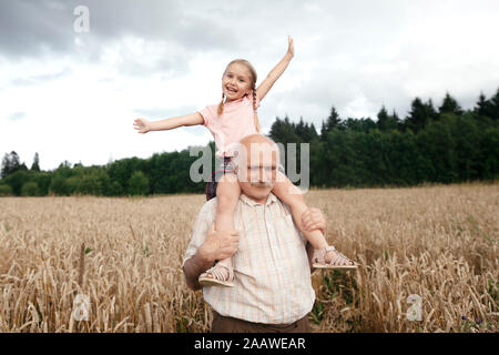 Portrait of happy little girl sur les épaules de grand-père dans un champ d'avoine Banque D'Images