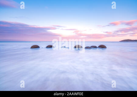 Moeraki Boulders en mer à Koekohe Plage contre le ciel au coucher du soleil, Nouvelle-Zélande Banque D'Images