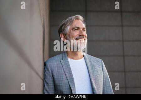 Le Portrait of smiling businessman leaning mature à la mode à un mur Banque D'Images
