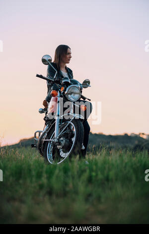 Jeune femme avec moto vintage scène rurale en appréciant le coucher du soleil Banque D'Images