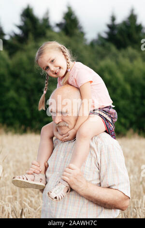 Portrait of happy little girl sur les épaules de grand-père dans un champ d'avoine Banque D'Images