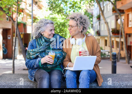 La haute mère avec son ordinateur portable à l'aide de sa fille adulte et de boire des jus dans la ville Banque D'Images