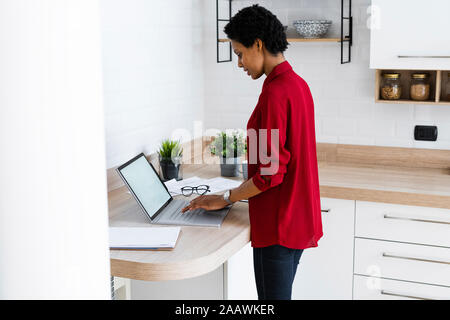 Young woman using laptop in cuisine à la maison Banque D'Images
