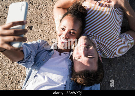 Happy young couple allongé sur un sol en béton en tenant un selfies Banque D'Images