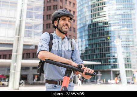 Smiling man with e-scooter sur city square, Berlin, Allemagne Banque D'Images