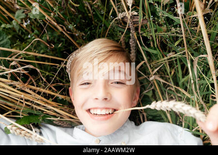 Portrait of smiling blond avec des oreilles d'avoine en bouche couché dans un champ d'avoine Banque D'Images