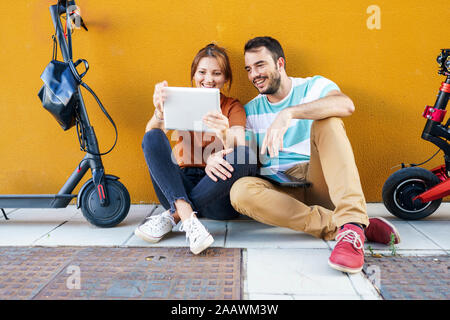 Portrait of smiling couple avec des scooters électriques using digital tablet Banque D'Images