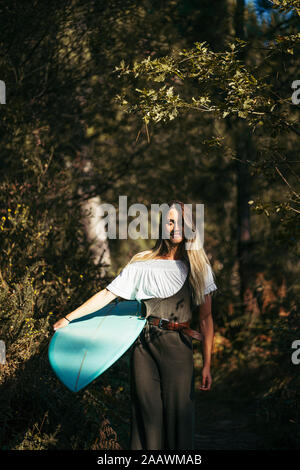 Jeune femme blonde avec un surf marcher en forêt Banque D'Images