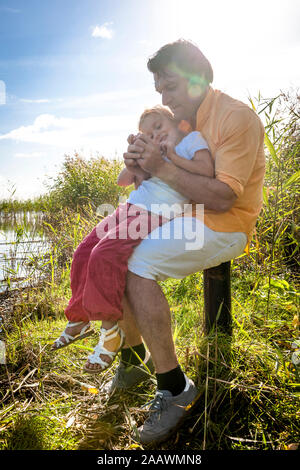 Père et fille assise sur poteau en bois à la côte, Darss, Mecklembourg-Poméranie-Occidentale, Allemagne Banque D'Images