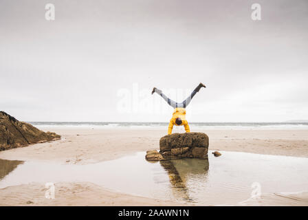 Jeune homme portant Veste pluie jaune sur la plage et faisant un headphones rock, Bretagne, France Banque D'Images