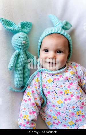 Baby Girl avec bunny hat et un lapin toy lying on bed Banque D'Images