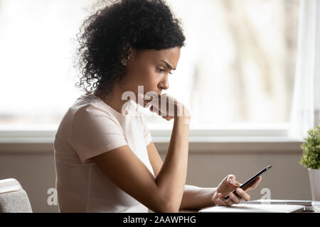 Pensive African American Woman perdue dans ses pensées using cellphone Banque D'Images