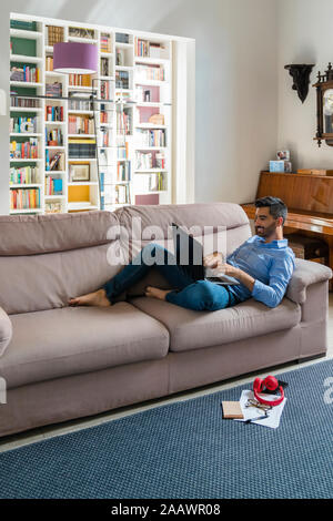 Jeune homme allongé sur la table à la maison à l'aide d'ordinateur portable Banque D'Images