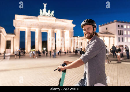 Jeune homme avec un scooter électrique à la porte de Brandebourg la nuit, Berlin, Allemagne Banque D'Images