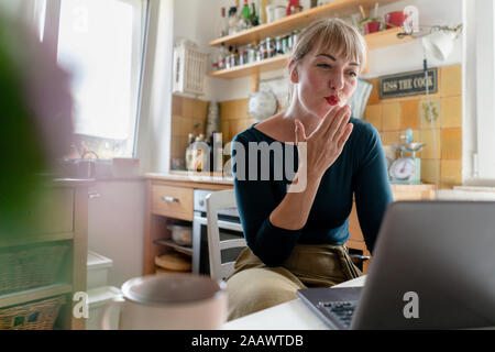 Portrait of young woman using laptop in La cuisine, soufflant un baiser Banque D'Images