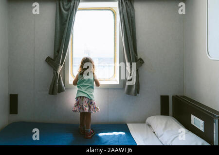 Vue de l'arrière petite fille debout sur le lit à la recherche de la mer depuis la fenêtre de la cabine du navire Banque D'Images