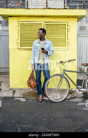 Jeune homme avec le smartphone, l'attente dans l'avant de la boîte jaune Banque D'Images