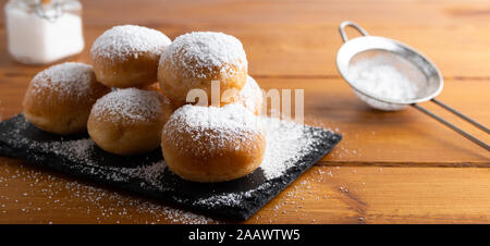 Des beignets sucrés frits recouverts de sucre sur une table en bois. Banque D'Images