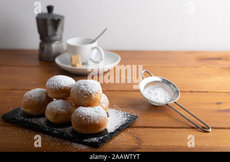 Des beignets sucrés frits recouverts de sucre sur une table en bois. Banque D'Images