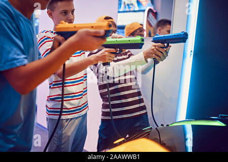 Amis adolescents tir avec des pistolets en une salle de jeux électroniques Banque D'Images