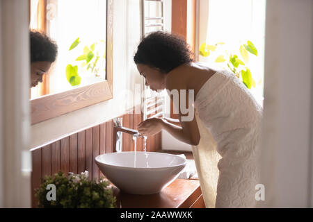 African American Woman visage de lavage dans une salle de bains moderne Banque D'Images