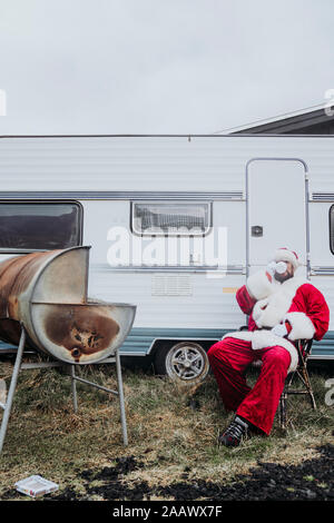 Le père Noël en train de préparer un barbecue en face d'un camping-car Banque D'Images